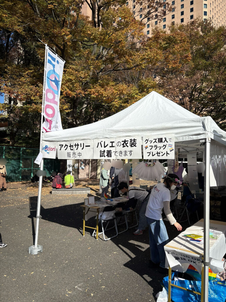 irOdoriブース全体像。irOdoriロゴののぼりが掲げられ「アクセサリー販売中」「バレエの衣装試着できます」「グッズ購入でフラッグプレゼント」のPOPが掲示されている。衣装のチュチュボンやトゥシューズ、レオタードのバレエアイテムの他、レインボーフラッグなどが見受けられる。